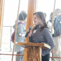Laura Aikens standing with microphone, talking to group